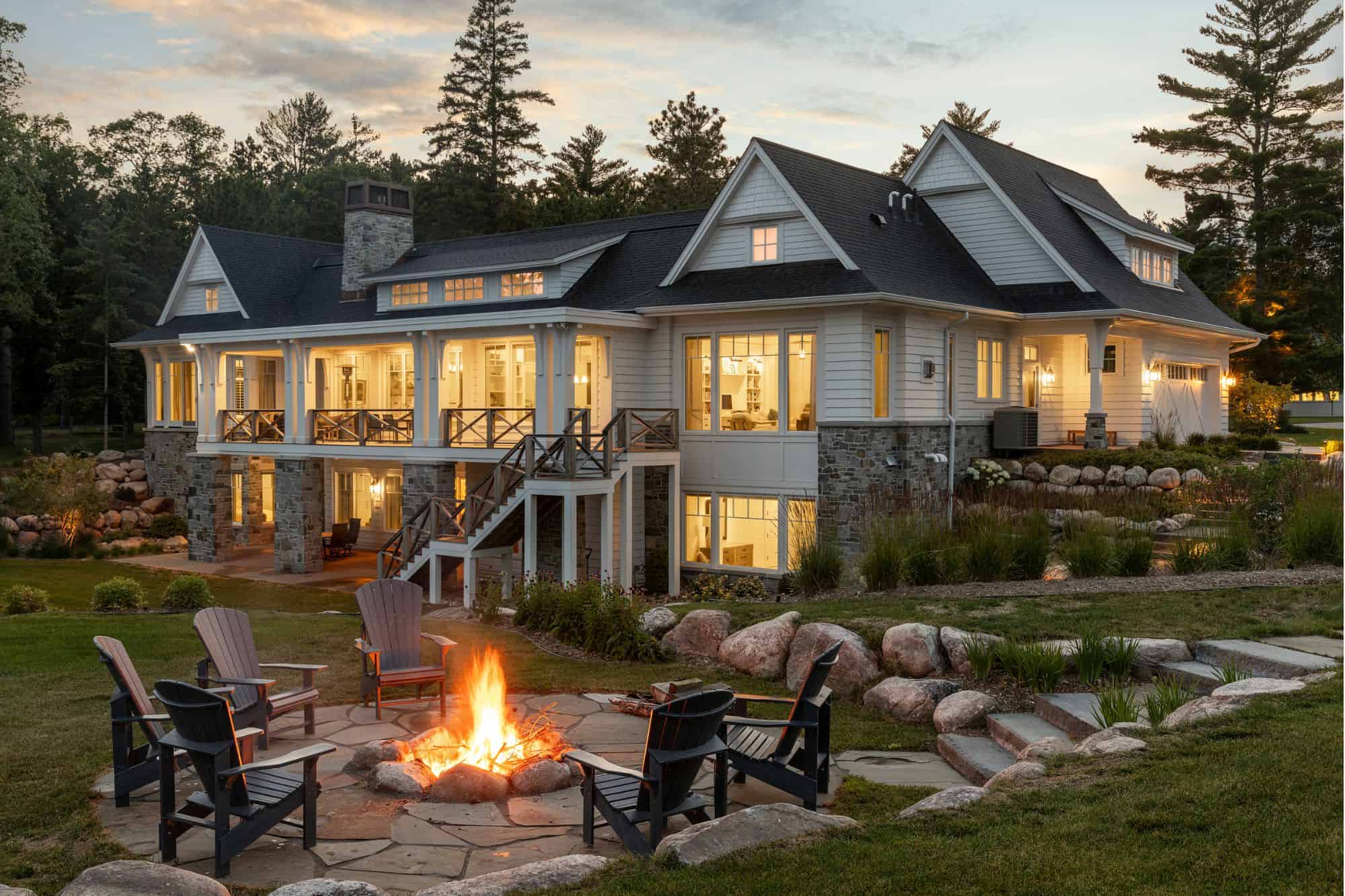 The picture shows a large, two-story house during the evening as the interior lights cast a warm glow.